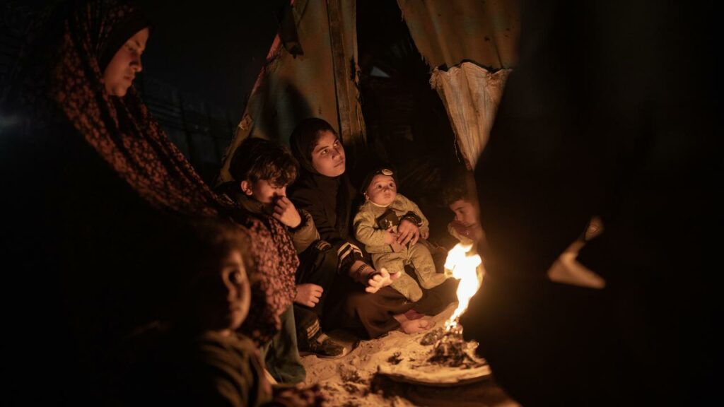 A displaced Palestinian family keep warm by a fire outside their tent in Rafah, in the Gaza Strip.
