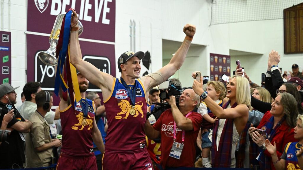 Brisbane tall Oscar McInerney proudly hoists the premiership cup in the changerooms after the game.
