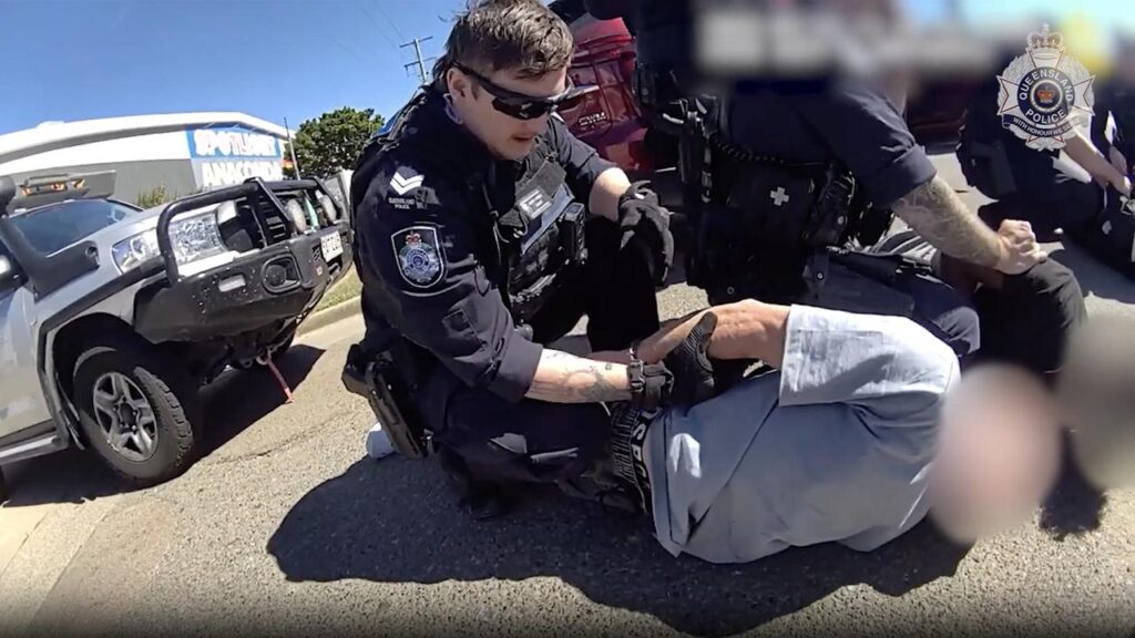 A police officer detains one of the suspects in a screenshot captured from a supplied video.
