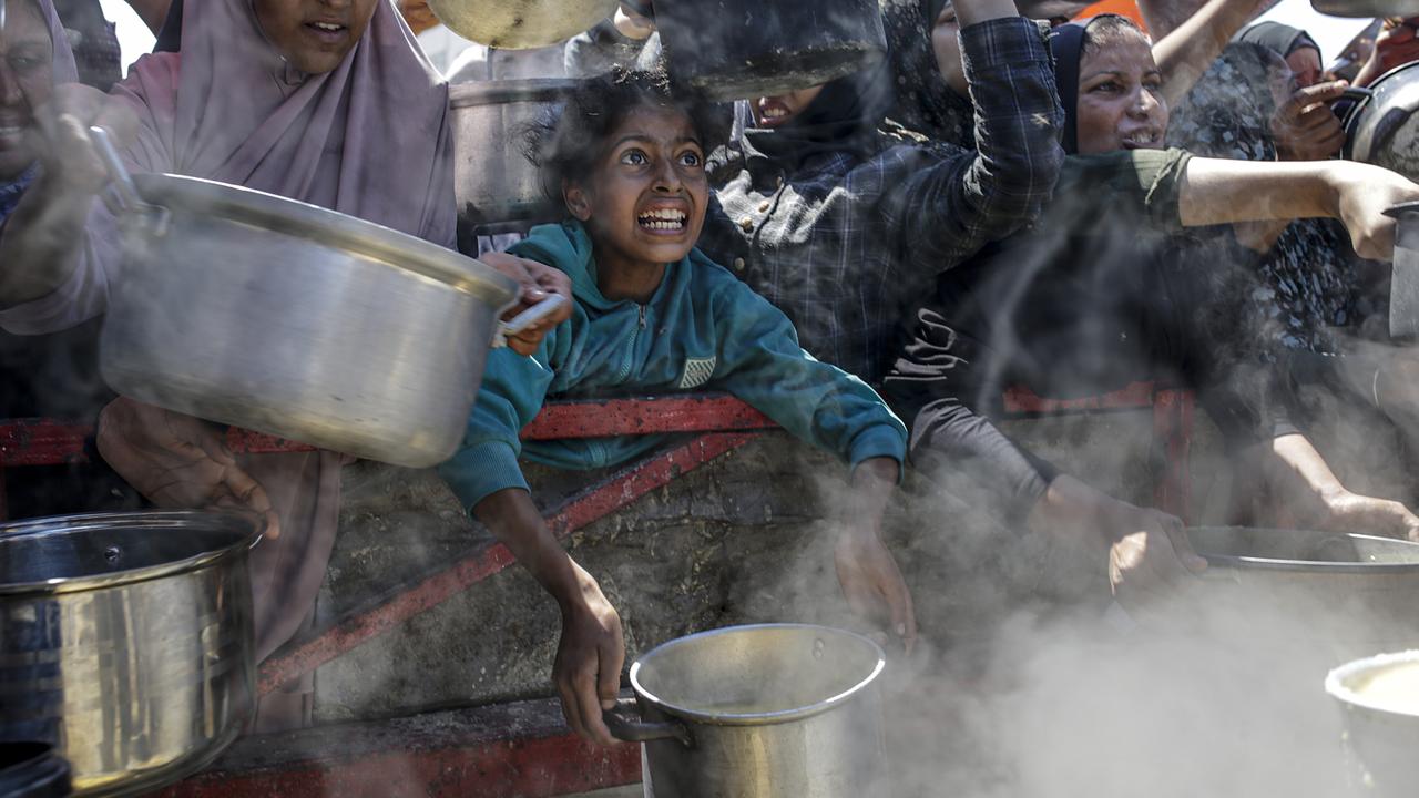Displaced Palestinian children hold pots as they receive food