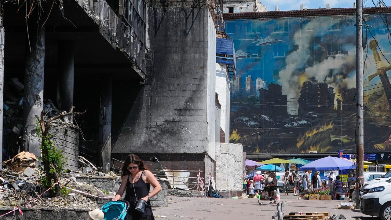A mother pushes a stroller past a damaged building in Kyiv