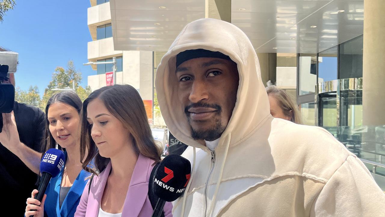 man looks at camera while walking past reporters