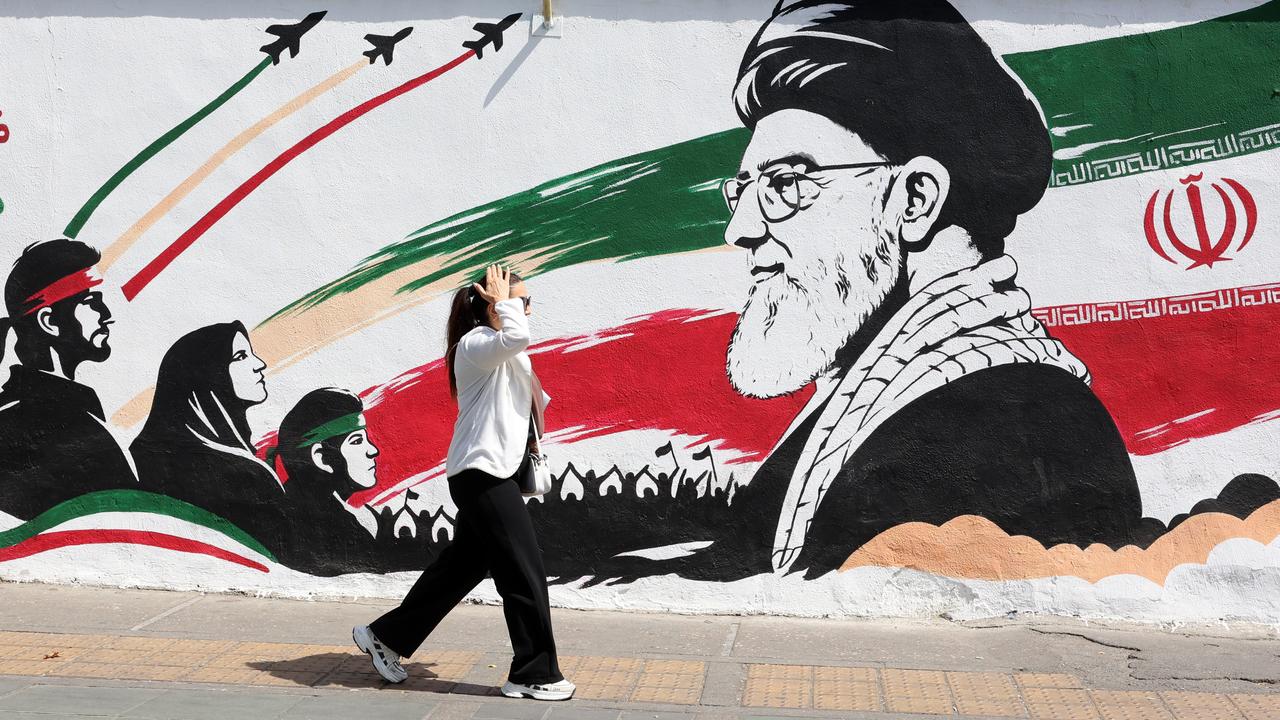 A woman walks past a mural in Tehran