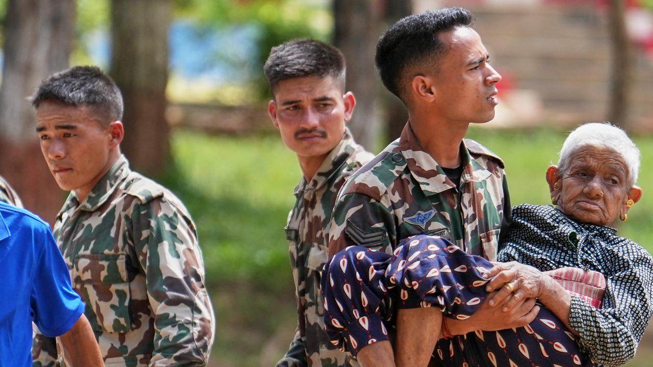 A soldier carries an elderly woman rescued by a helicopter