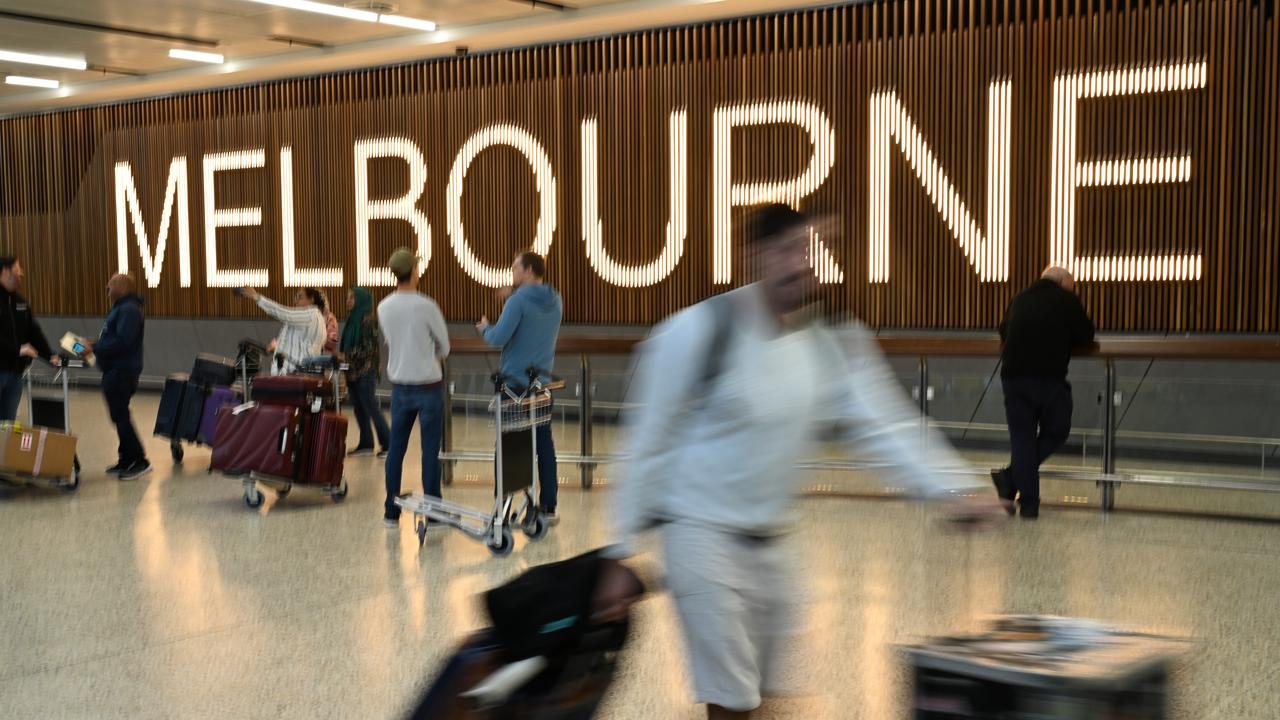 Travellers pass by the Melbourne sign at the airport