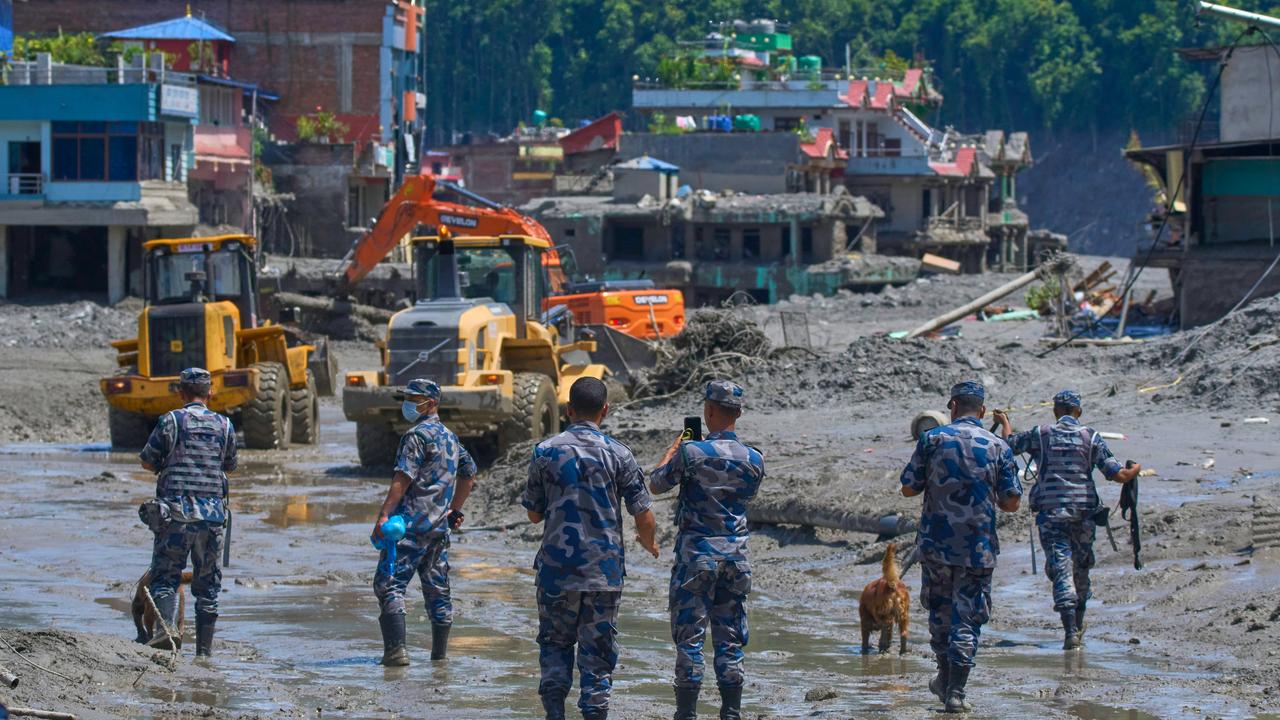 Nepalese policemen watch as earthmovers clear flood debris in Nepal