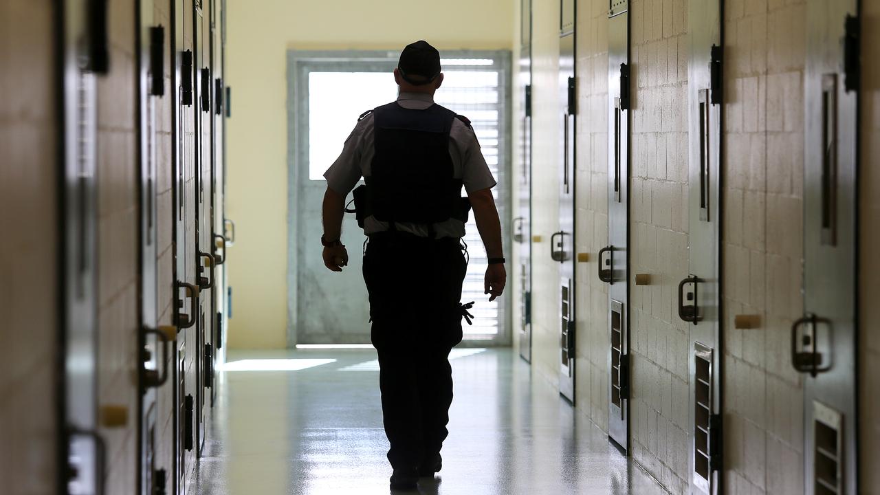 A corrections officer walks down a cell corridor.