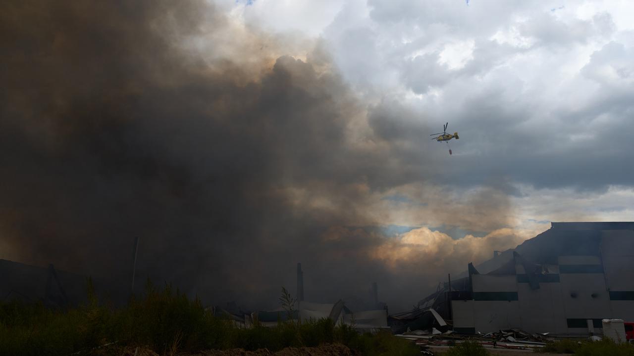 A helicopter drops water to extinguish a fire in a destroyed warehouse