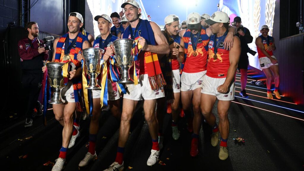 Josh Dunkley, Hugh McCluggage and Harris Andrews proudly carry the Lions’ three premiership cups.
