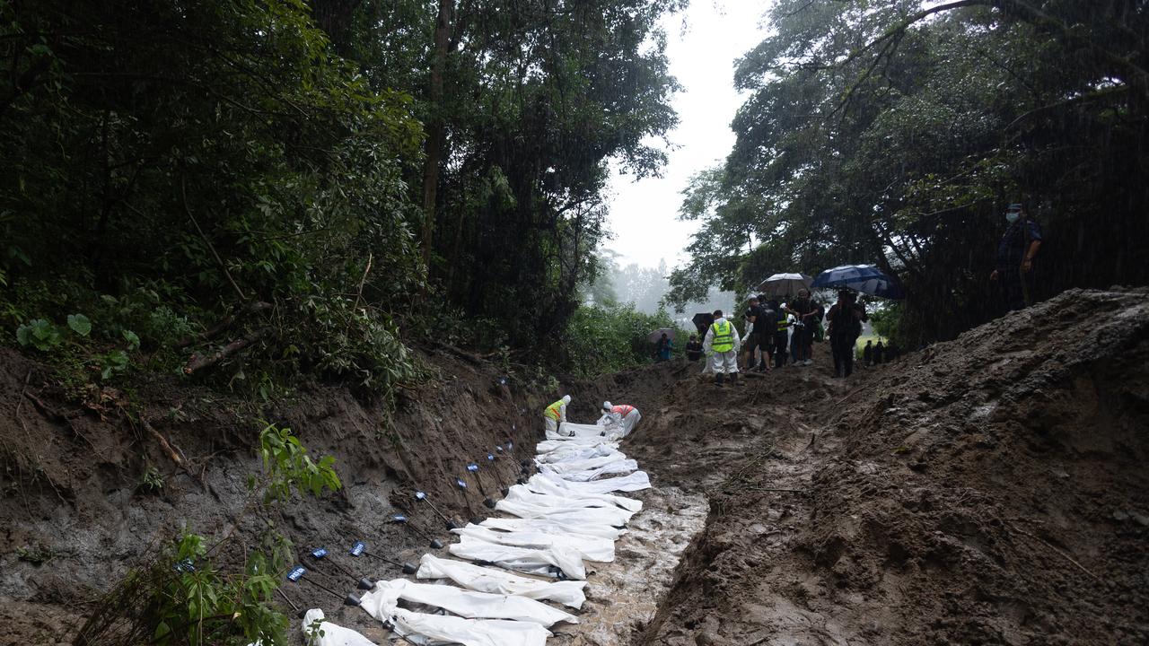 Officers place the bodies of unidentified victims into a mass grave