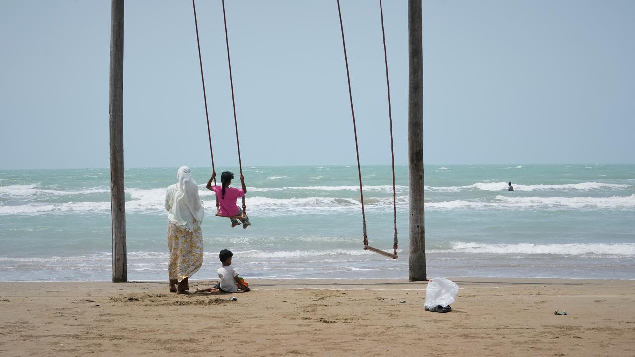 A woman pushes a girl on a swing on a beach